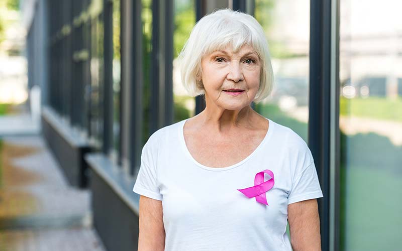 senior woman with white shirt wearing a breast cancer awareness ribbon