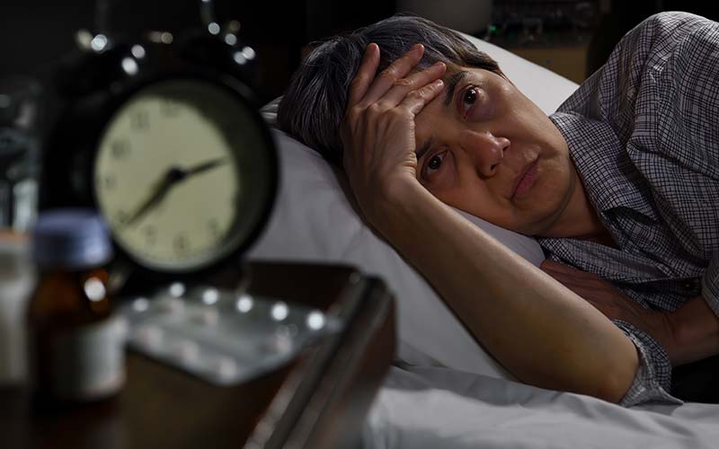 woman in bed next to medicine unable to sleep