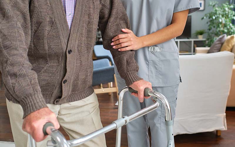 nurse helping a man walk with a walker