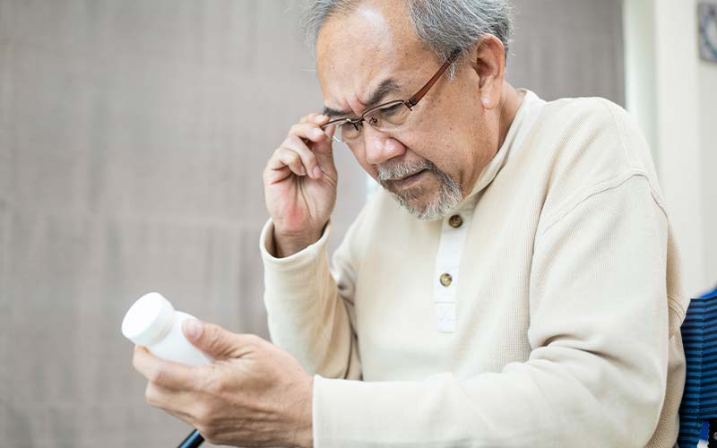 elderly man wearing glasses having trouble reading medication bottle