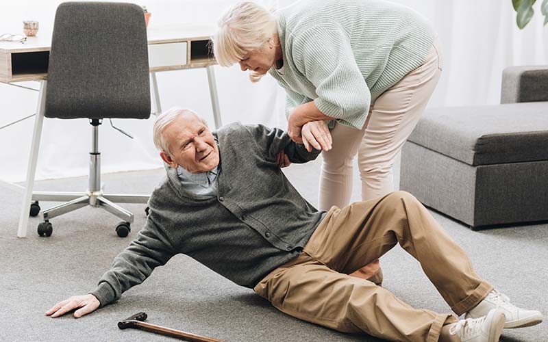 senior man being helped up off the floor by his elderly wife after a fall