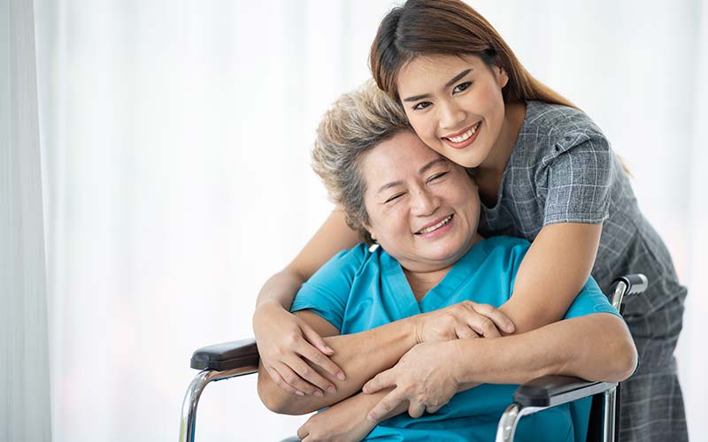 smiling daughter hugging mother who is in a wheelchair while home for the holidays