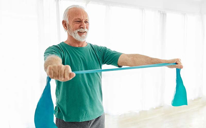 an elderly man in private pay rehab is using resistance bands to increase strength