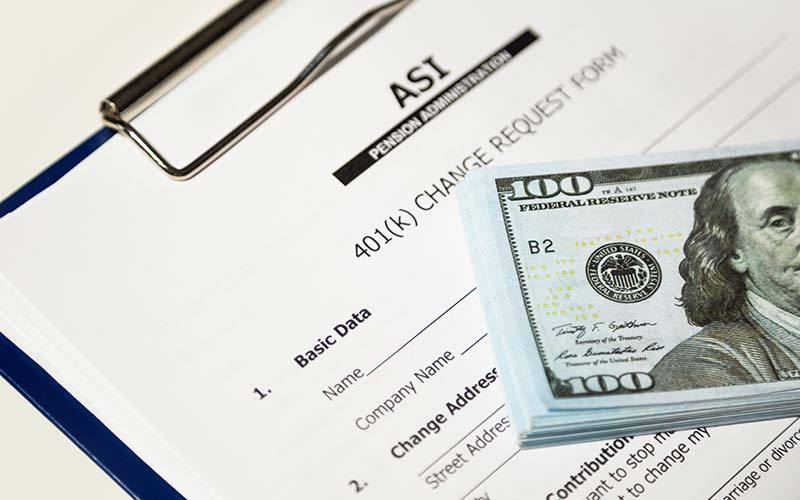 A 401k document next to a stack of $100 bills
