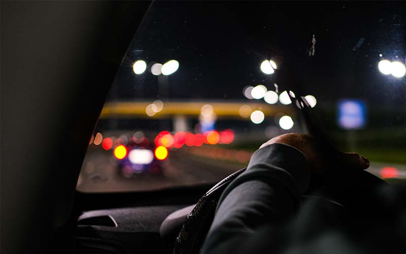 a view of a street at night from behind the steering wheel inside the car