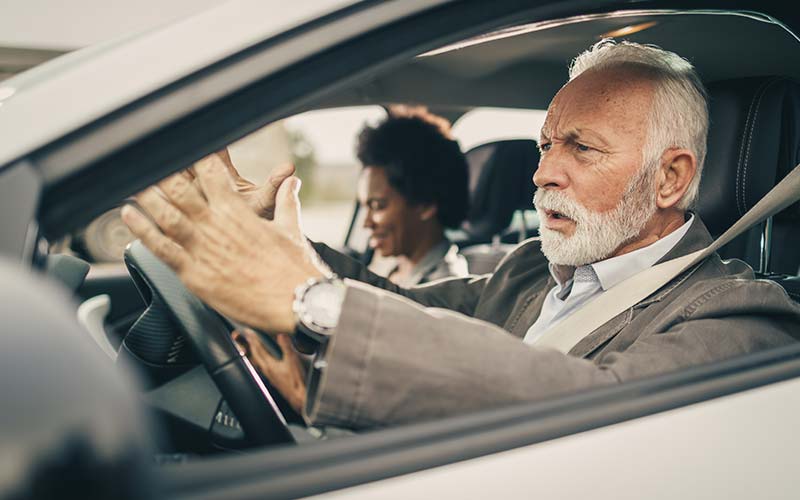 elderly man driving holding his hands up over the steering wheel, visibly frustrated with other drivers as a sign dad shouldn't drive anymore