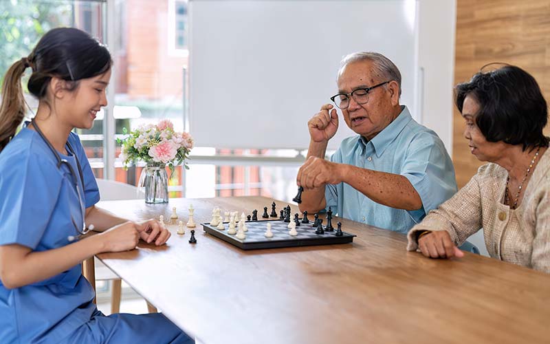 senior couple plays chess with a female memory care nurse