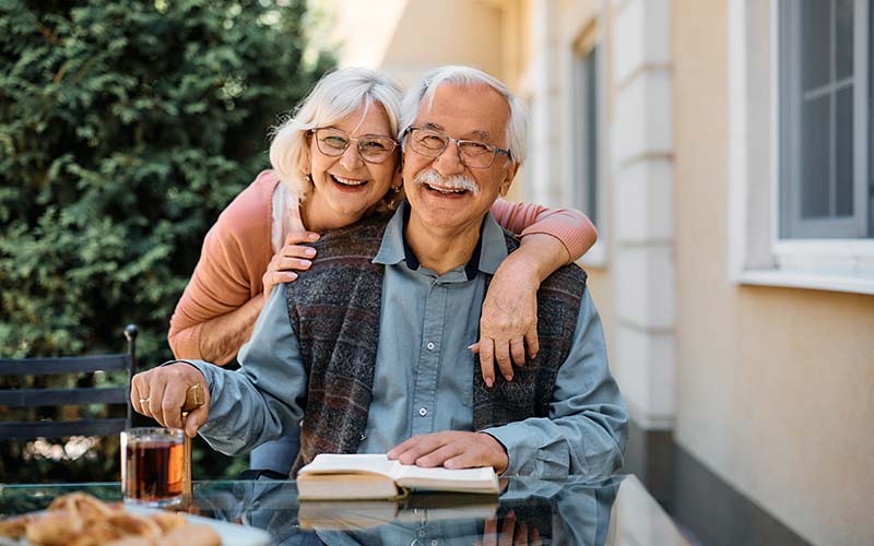 a smiling senior couple sitting out side their independent living community