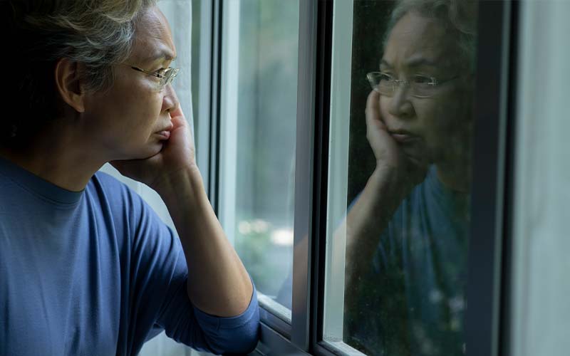 a depressed woman stares out a window to highlight the mental strain elder abuse can take