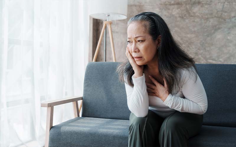 a senior woman having a panic attack highlighting it as a sign of elder abuse, alone on the couch