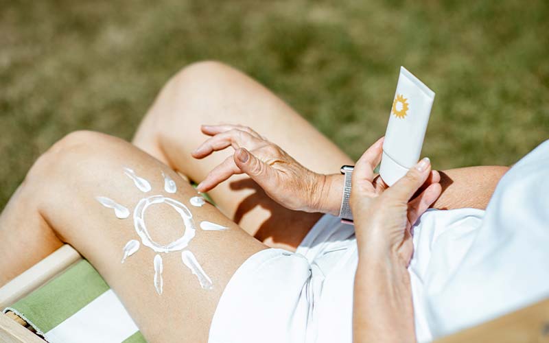 a senior woman applies sunblock painted like a sun on her leg to avoid uv rays