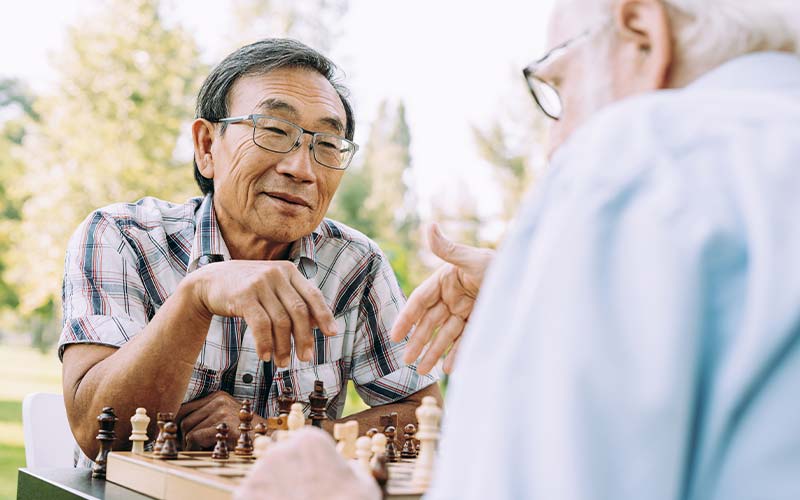two senior men socializing while playing a game of chess outdoors