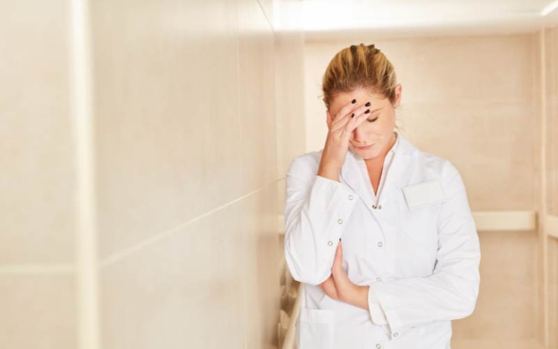 a nurse caregiver stands in a facility hallway holding her forehead having a hard time managing stress stress