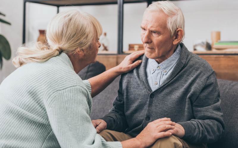 a wife consoles her husband as he appears to be displaying stages of dementia